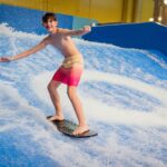 Boy in red shorts rides board on water in a waterpark ride.
