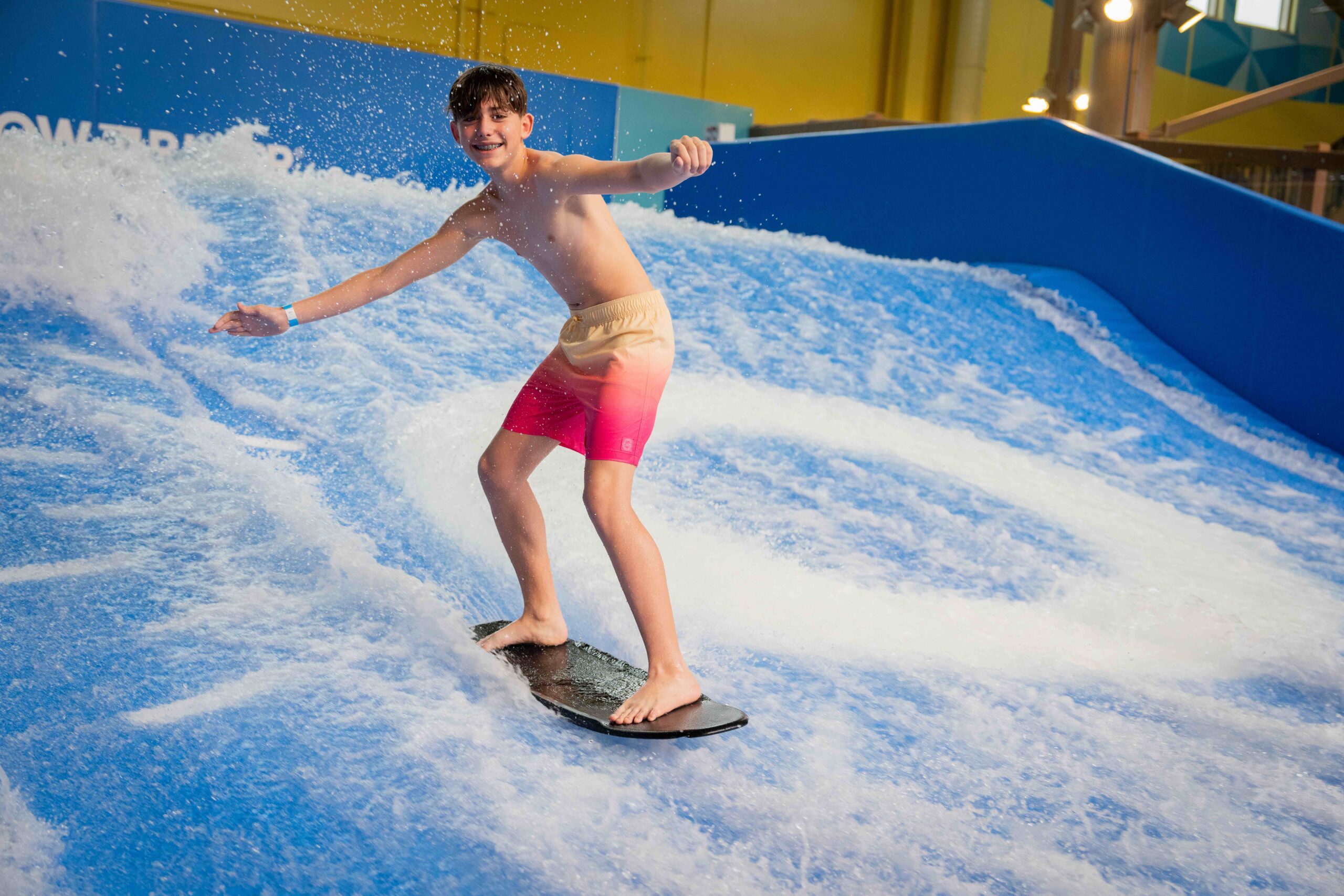 Boy in red shorts rides board on water in a waterpark ride.